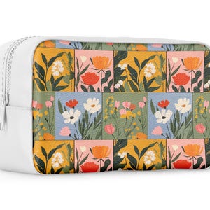 May include: White zippered pouch with a floral pattern. The pattern features a variety of flowers in shades of pink, orange, yellow, blue, and green. The flowers are arranged in a patchwork design.