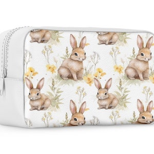 May include: White zippered pouch with a repeating pattern of brown bunnies and yellow flowers on a white background.