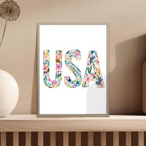 Watercolor floral letters spelling "USA" in a framed print.