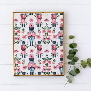 May include: A framed print with a repeating pattern of nutcracker soldiers and pink flowers. The print has a white background and a gold frame.