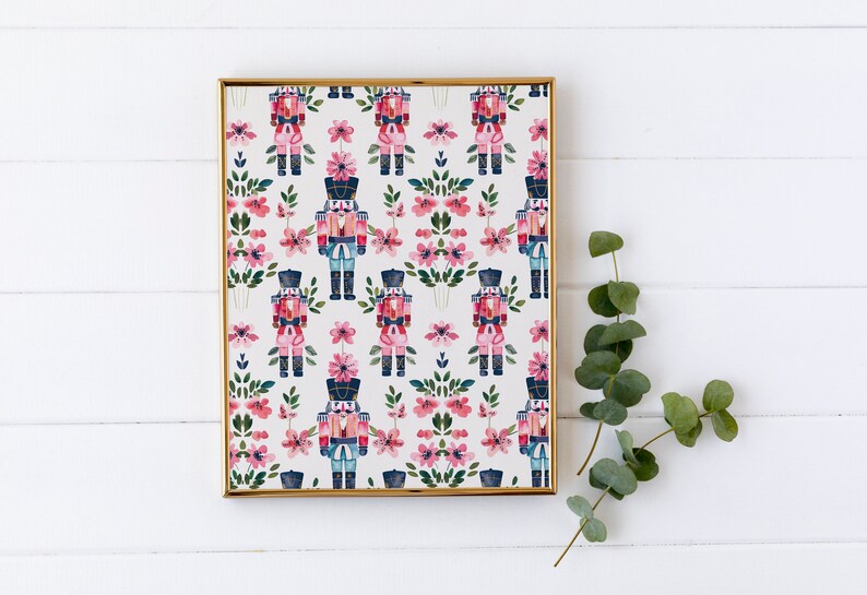 May include: A framed print with a repeating pattern of nutcracker soldiers and pink flowers. The print has a white background and a gold frame.