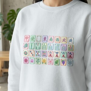 Mahjong tiles printed on a white sweatshirt, featuring Chinese characters and numbers.