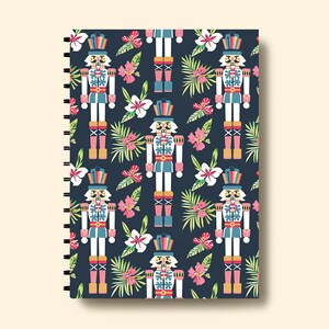 Pu&ograve; includere: Una copertina per quaderno blu scuro con un motivo ripetuto di soldati schiaccianoci colorati e fiori tropicali.