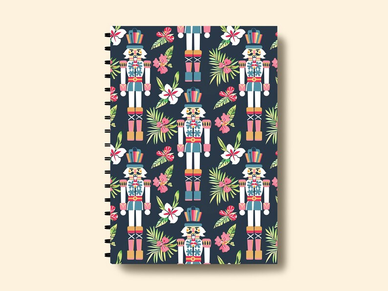 Pu&ograve; includere: Una copertina per quaderno blu scuro con un motivo ripetuto di soldati schiaccianoci colorati e fiori tropicali.