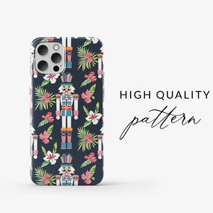 Pu&ograve; includere: Una custodia per telefono con un motivo ripetitivo di schiaccianoci e fiori tropicali su uno sfondo blu scuro. Gli schiaccianoci indossano cappelli colorati e hanno un design fantasioso. I fiori sono rosa e bianchi con foglie verdi.