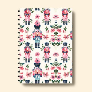 May include: A white spiral bound notebook with a repeating pattern of pink flowers and watercolor nutcracker soldiers.