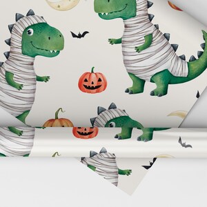 May include: White wrapping paper with a repeating pattern of green mummies dressed as dinosaurs, orange pumpkins with jack-o-lantern faces, and black bats.