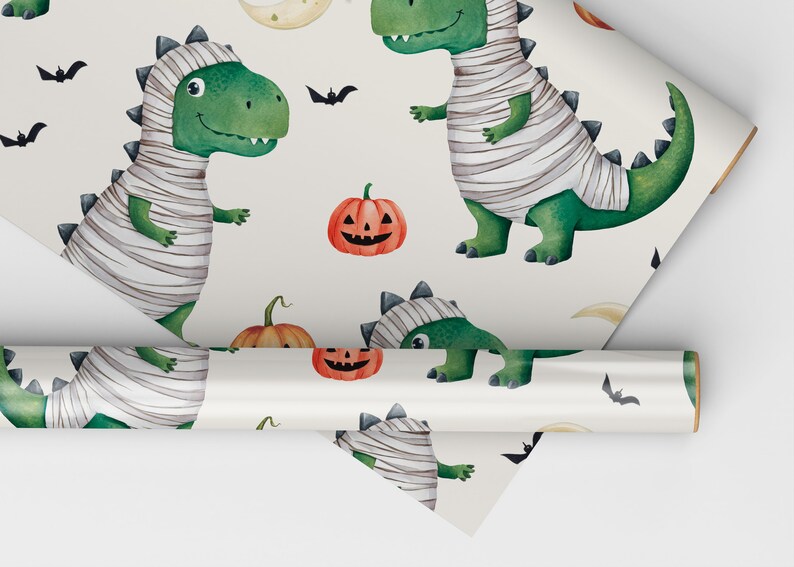 May include: White wrapping paper with a repeating pattern of green mummies dressed as dinosaurs, orange pumpkins with jack-o-lantern faces, and black bats.
