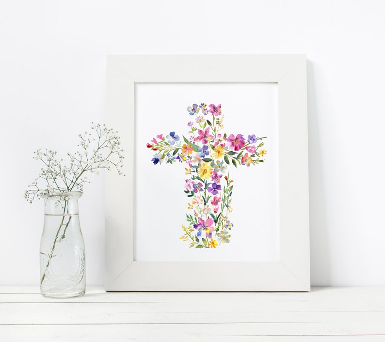 May include: A white framed print with a watercolor painting of a cross made of colorful flowers. The flowers are in shades of pink, purple, yellow, and blue.