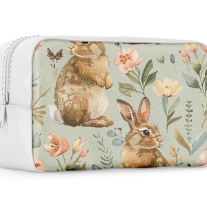 May include: White zippered pouch with a floral pattern featuring brown rabbits and butterflies on a light green background.