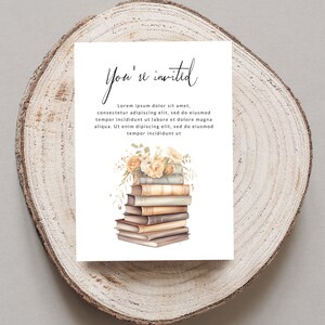 May include: A white card with the text "You're invited" in black cursive script. The card features a watercolor illustration of a stack of vintage books with a bouquet of cream-colored roses on top.