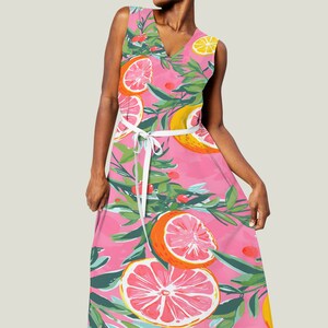 May include: A pink sleeveless maxi dress with a white tie belt. The dress features a colorful print of lemons, grapefruits, and green leaves.