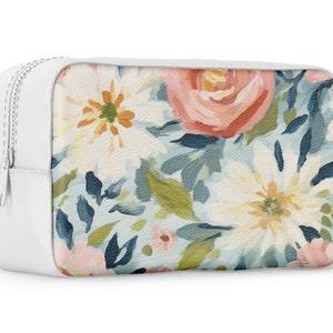 May include: White zippered pouch with a floral print featuring pink, white, and blue flowers on a light blue background.