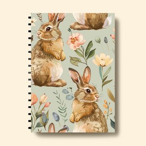 May include: A spiral bound notebook with a green cover featuring a repeating pattern of brown rabbits and watercolor flowers.