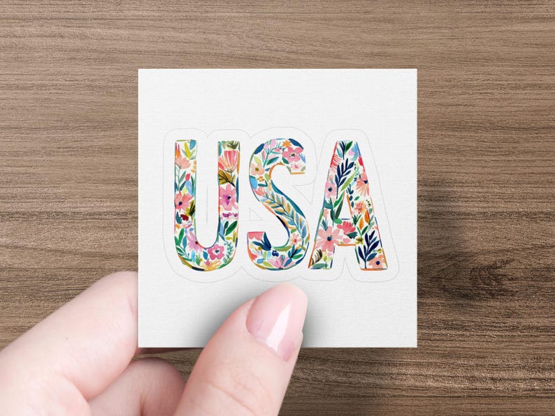 Sticker with floral letters spelling "USA" held by a hand.