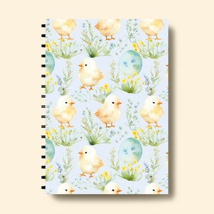 May include: A spiral bound notebook with a light blue cover featuring a repeating pattern of yellow chicks, blue eggs, and green foliage.