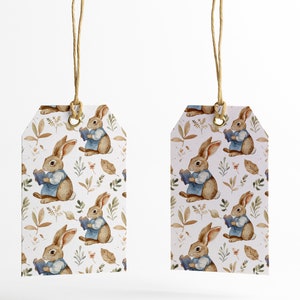 May include: Two white gift tags with brown twine hanging from the top. The tags are decorated with a repeating pattern of brown rabbits holding books, green leaves, and brown leaves.