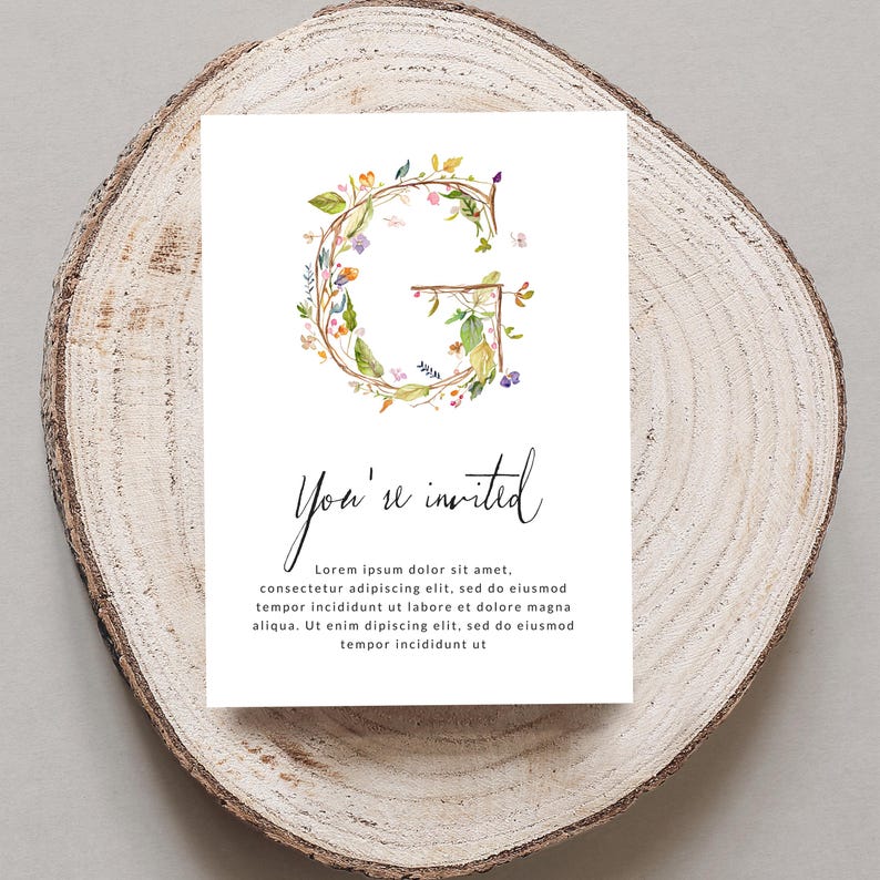 May include: A white invitation card with a floral wreath in shades of green, yellow, and pink forming the letter "G". The text "You're invited" is written in black cursive script below the wreath. The text "Lorem ipsum dolor sit amet, consectetur adipiscing elit, sed do eiusmod tempor incididunt ut labore et dolore magna aliqua. Ut enim dipiscing elit, sed do eiusmod tempor incididunt ut" is written in black below the cursive text.