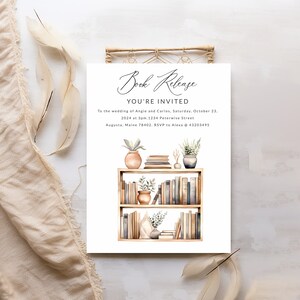 May include: A wedding invitation with a watercolor illustration of a bookshelf filled with books, plants, and decorative items. The text reads "Book Release You're Invited To the wedding of Angie and Carlos, Saturday, October 23, 2024 at 3pm. 1234 Peterwise Street Augusta, Maine 78402. RSVP to Alexa @ 43203495"