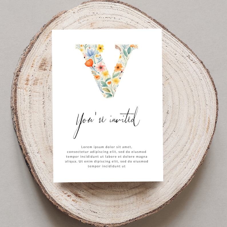 May include: A white card with a floral letter V and the text "You're invited". The card is on a wooden surface.