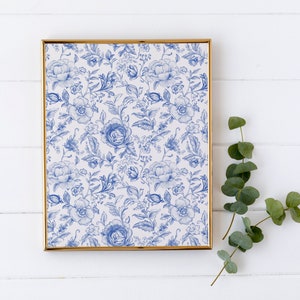 May include: A framed print with a blue and white floral pattern. The print is in a gold frame and is hanging on a white wall.