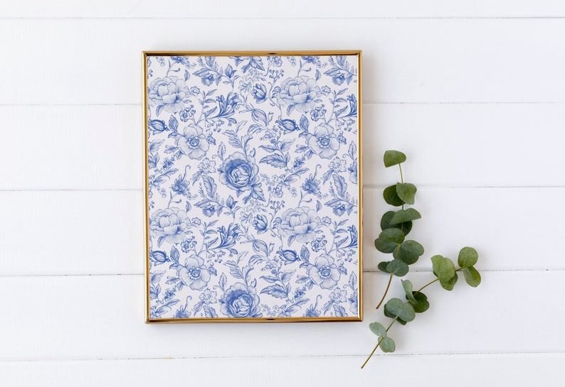 May include: A framed print with a blue and white floral pattern. The print is in a gold frame and is hanging on a white wall.
