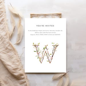 May include: Wedding invitation with a floral letter W design. The invitation reads "You're Invited" to the wedding of Angie and Carlos on Saturday, October 23, 2024 at 3pm. 1234 Peterwise Street, Augusta, Maine 78402. RSVP to Alexa @ 43203495.