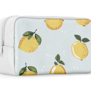Puede incluir: Bolsa blanca con cremallera, fondo azul claro y un patr&oacute;n repetido de limones amarillos con hojas verdes.