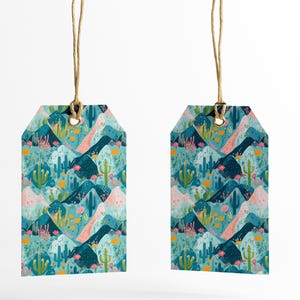 May include: Two turquoise blue gift tags with a repeating pattern of pink and blue mountains, green cacti, and yellow flowers. The tags are hanging from twine.