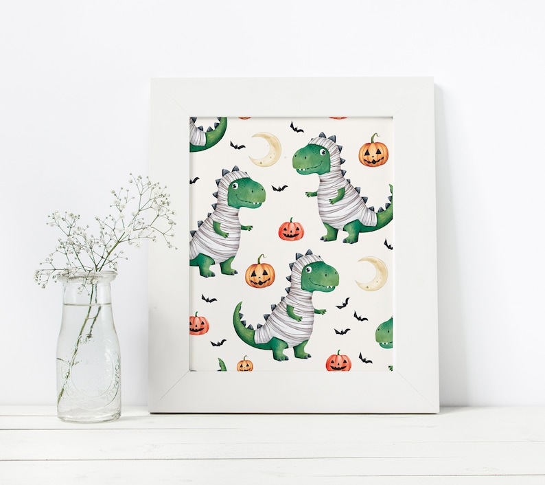 May include: A white framed print with a repeating pattern of green mummies, orange pumpkins, and black bats on a white background. The mummies are dinosaurs wearing white bandages.