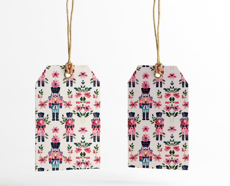 May include: Two white gift tags with a repeating pattern of pink flowers and nutcracker soldiers. The tags are tied with twine.