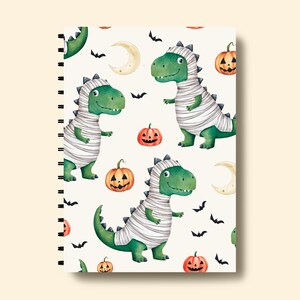 May include: A white spiral bound notebook with a Halloween themed pattern. The pattern features green and white mummies, orange pumpkins, and black bats on a white background.