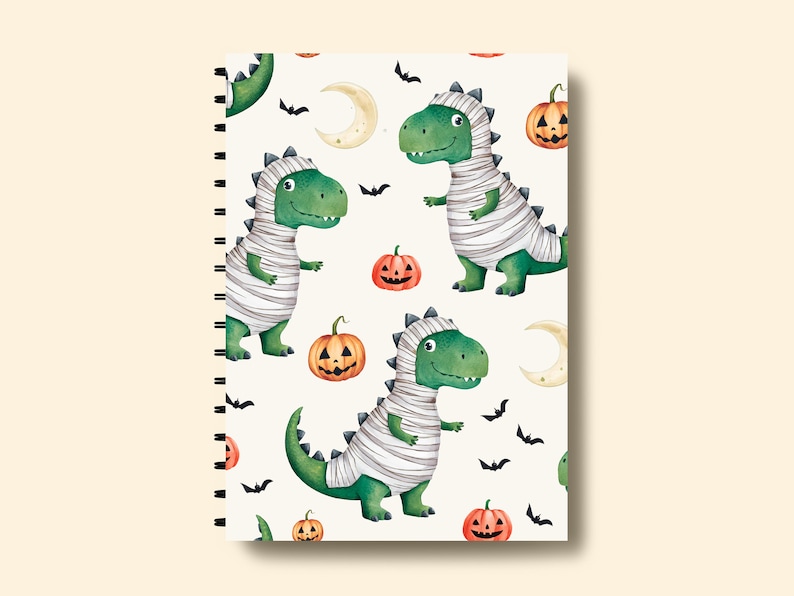 May include: A white spiral bound notebook with a Halloween themed pattern. The pattern features green and white mummies, orange pumpkins, and black bats on a white background.