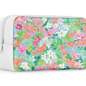 K&ouml;nnte beinhalten: Eine wei&szlig;e Rei&szlig;verschlusstasche mit einem Blumenmuster. Der Druck zeigt rosa, orange, wei&szlig;e und gr&uuml;ne Blumen auf hellblauem Hintergrund.