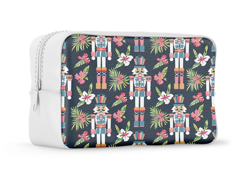 Pu&ograve; includere: Borsa bianca con cerniera con sfondo blu e un motivo ripetuto di figure di schiaccianoci, foglie tropicali e fiori rosa.