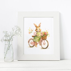 Op de afbeelding: Een aquarel-illustratie van een bruin konijn dat op een roze fiets rijdt met een mand vol bloemen. Het konijn draagt een groene jurk en een roze shirt.