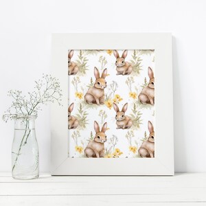 May include: A white framed print with a repeating pattern of brown rabbits and yellow flowers on a white background.