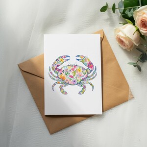 Watercolor crab illustration with floral pattern on card atop brown envelope with roses.