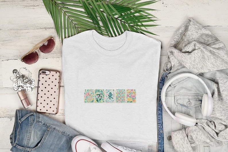 White t-shirt with floral patterned squares on chest, styled with jeans, hoodie, and headphones.