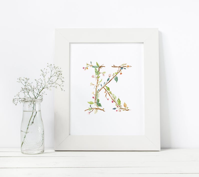 May include: A white frame with a white mat surrounding a print of the letter K made of green leaves and pink flowers.