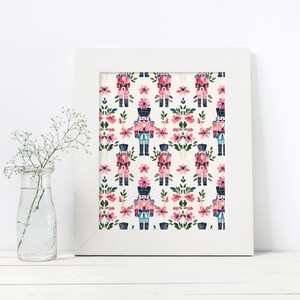 May include: A white framed print with a repeating pattern of pink flowers and blue and red nutcracker soldiers on a white background.