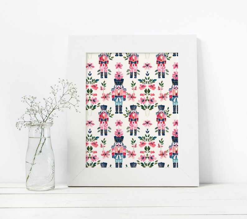 May include: A white framed print with a repeating pattern of pink flowers and blue and red nutcracker soldiers on a white background.