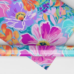 Pu&ograve; includere: Un rotolo di carta da regalo con un motivo floreale colorato. La carta presenta grandi fiori rosa, viola e blu con accenti arancioni e verdi su uno sfondo blu chiaro.
