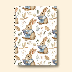 May include: A white spiral bound notebook with a repeating pattern of brown rabbits reading books, brown leaves, and green foliage.