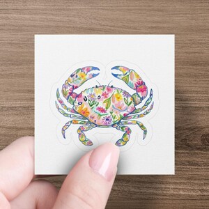 Floral crab sticker held by a hand against a wooden background.