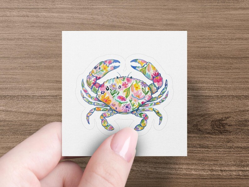 Floral crab sticker held by a hand against a wooden background.