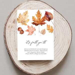 May include: Autumn wedding announcement featuring a watercolour illustration of autumn leaves in shades of orange, red, and yellow. The text reads "It's fall ya'll" and includes the couple's names, wedding date, and RSVP details.