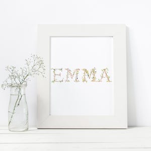 May include: White framed print with the name "EMMA" spelled out in green, pink, and white floral letters.