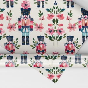 May include: White wrapping paper with a repeating pattern of pink flowers and blue and red nutcracker soldiers. The nutcrackers are wearing gold hats and have gold accents.