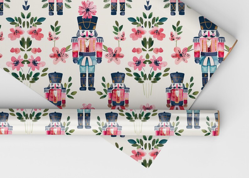 May include: White wrapping paper with a repeating pattern of pink flowers and blue and red nutcracker soldiers. The nutcrackers are wearing gold hats and have gold accents.